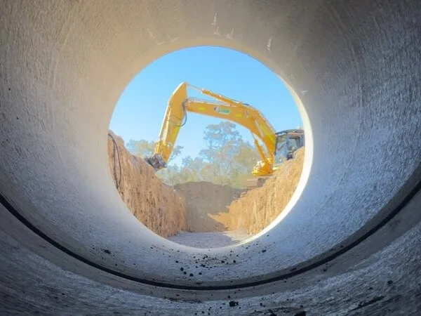 Excavator viewed through a concrete pipe on a civil works site